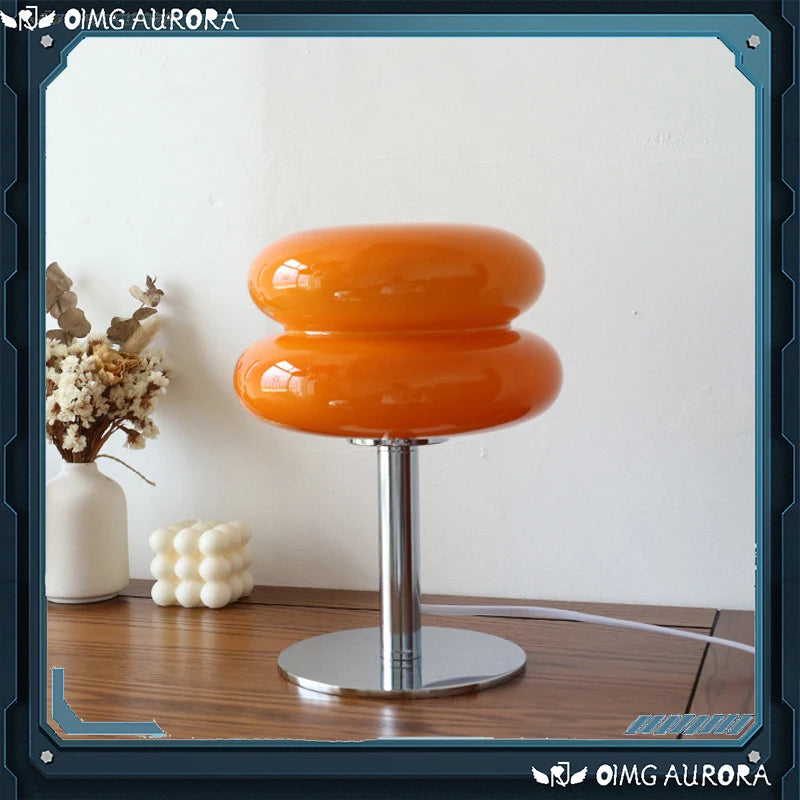 Small tinted glass macaron table lamp glowing warm on a bedside table
